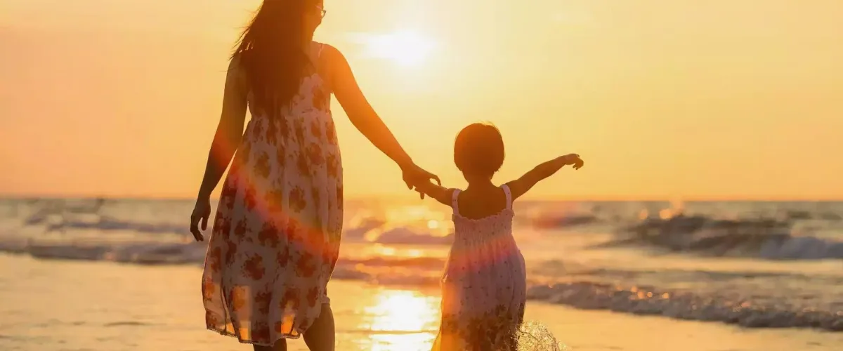 Madre e hija de la mano durante la puesta de sol en la playa